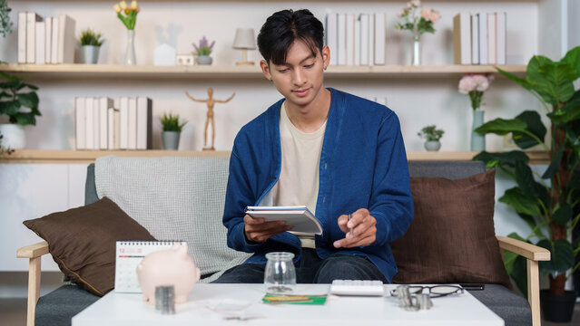 Asian man budgeting personal finance and saving money with piggy bank at home