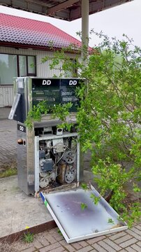 Abandoned DD fuel pump with exposed mechanics and overgrown bushes at former gas station