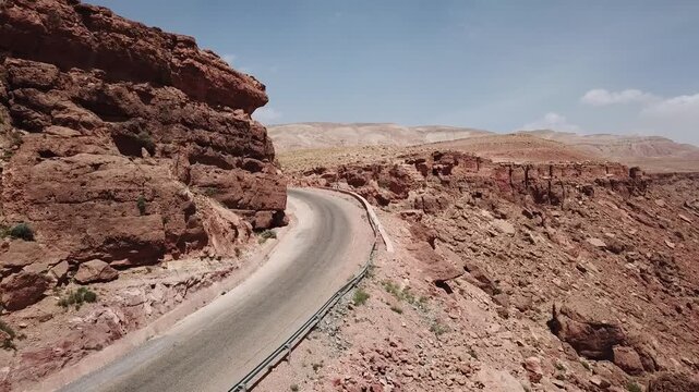 Aerial drone footage of a winding mountain road cutting through rugged desert terrain in Morocco. Strong leading lines and dramatic rocky environment create a cinematic driving experience ideal for tr
