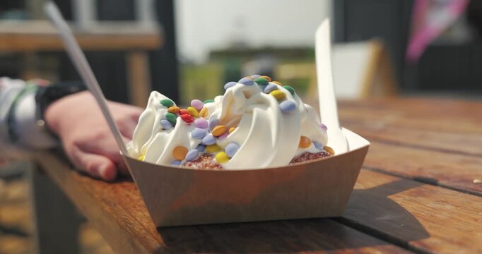 Slow motion close up of a donut dessert topped with ice cream and colourful sprinkles on an outdoor table near Littlehampton seafront