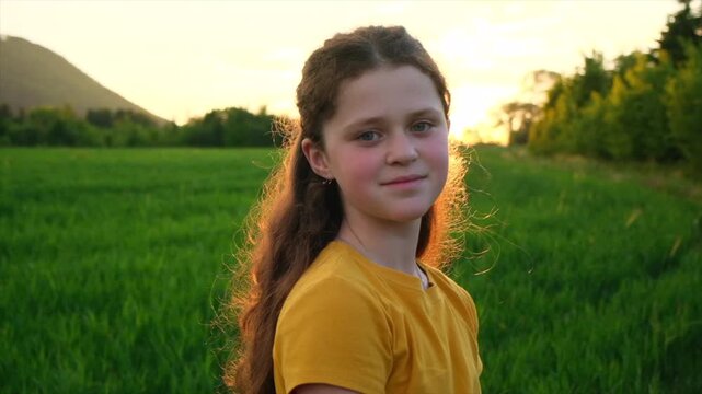 Portrait of smiling charming pretty preteen girl in park at summer warm day. Adorable happy child is dreaming looking at camera. Children day. Childhood and nature concept