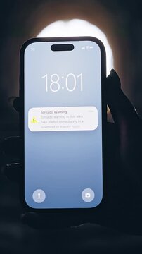 Vertical video. Smartphone Displaying Tornado Warning Notification Inside Dark Tunnel With Bright Backlight, Cinematic Emergency Scene About Extreme Weather and Survival