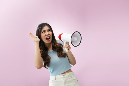 Worried Indonesian woman holding megaphone with shocked and anxious expression on pink background, representing panic, bad news, emergency announcement, and stressful situation concept.