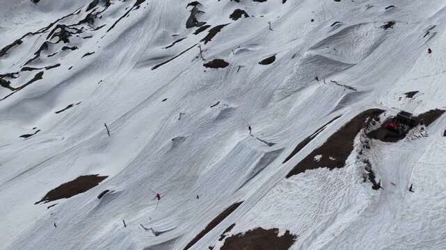 Drone view of snowboarders and skiers performing tricks on big air kickers in Tignes snowpark during sunny spring day in the French Alps. Freestyle snowboard and ski session on big air jumps in alps