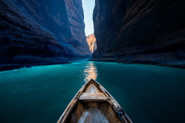 Fototapeta premium Small weathered wooden boat navigating a wide river, entering a canyon with towering rock walls and soft cyan water glow illuminating the scene ahead