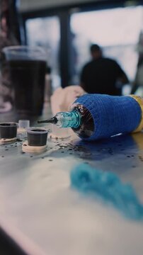 A tattoo machine with blue and yellow grip tape rests next to cups of black ink. The professional equipment is ready for a new tattooing session.