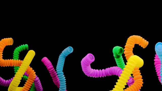 A colorful arrangement of stretchy ribbed colorful plastic flexible tubes against a black background, These are colorful plastic sensory fidget tubes designed for tactile stimulation and stress relief