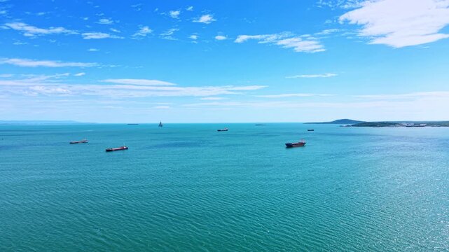 Industrial cargo ships floating in turquoise sea water. Aerial perspective of multiple red and blue bulk carriers distributed across calm turquoise sea.