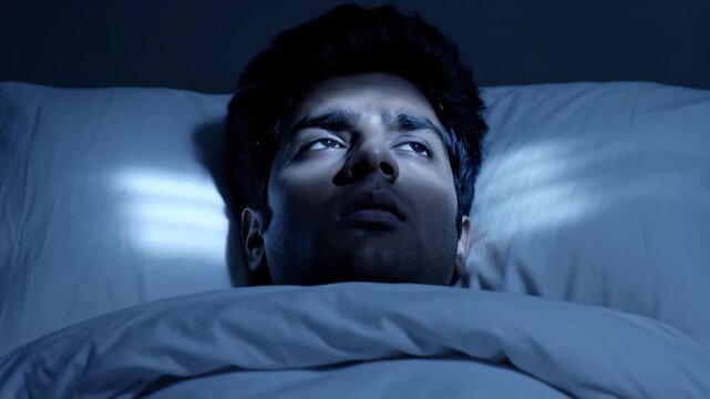 A young man lies beneath soft sheets, gazing thoughtfully into the distance as subtle blue light dances across his face, creating a serene yet evocative atmosphere filled with dreams and wonder.