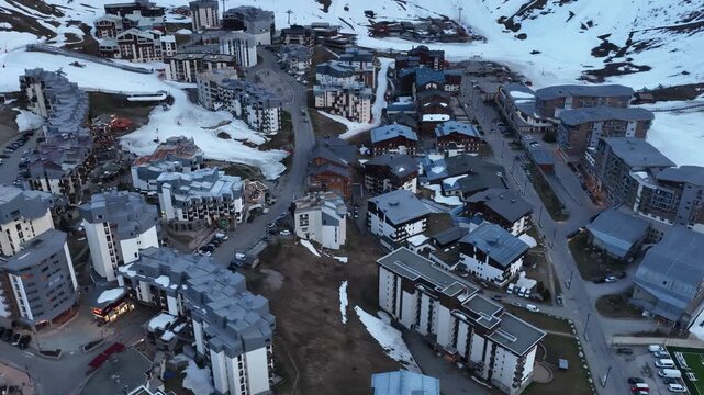 Evening drone view of Tignes 2100 in the French Alps, showing illuminated mountain resort buildings and hotels surrounded by dramatic alpine peaks under twilight sky atmosphere