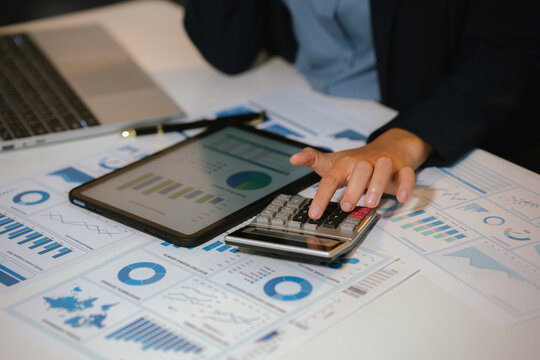 Business professional analyzing financial charts and using calculator for accounting, budgeting, and corporate financial planning at office desk.