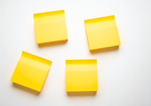 Four bright yellow adhesive memo pads lying scattered on a crisp white surface, ready for notes, reminders, and creative brainstorming