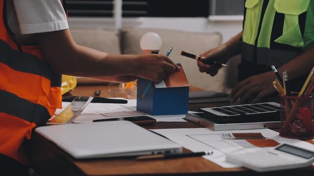 Two engineers are analyzing blueprints and working on a laptop in their office container, discussing the progress of their construction project