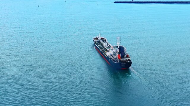 Aerial tracking shot of oil tanker leaving wake. High angle rear view of chemical tanker ship sailing in turquoise water leaving white foam wake.