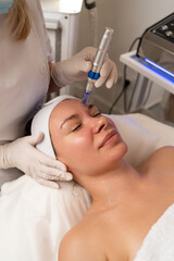 Fototapeta premium Woman undergoing microneedling procedure on face in a cosmetology clinic