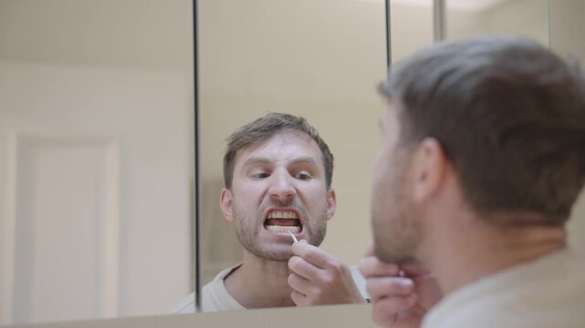 Over the shoulder view of a man looking in the bathroom mirror while flossing his teeth