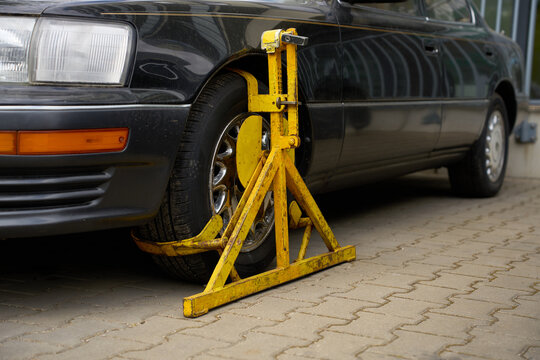 Heavy-duty yellow wheel clamp attached to the front tire of a black car on a city street.
