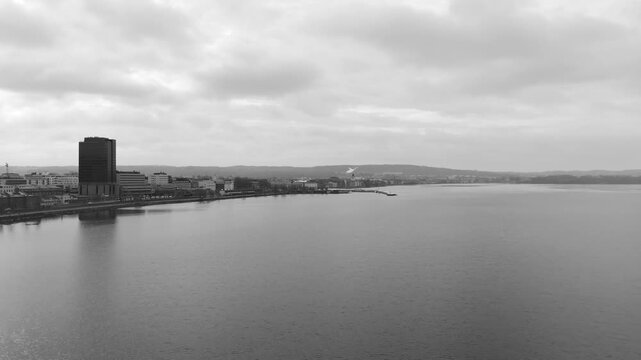 Black and white aerial drone shot of Jonkoping showing city skyline along Lake Vattern with calm water and cloudy sky creating minimal urban waterfront scene