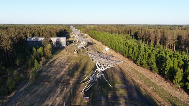 Aerial view of the westerbork synthesis radio telescope array in a forest clearing in the netherlands at sunset, satellite dishes casting long shadows across the landscape