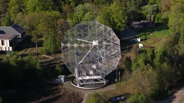Aerial circling shot of the historic dwingeloo radio telescope, a scientific astronomical instrument surrounded by lush green woodland scenery in the netherlands national park