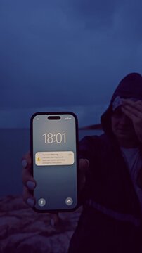 Vertical Shot of Woman Facing Strong Wind While Holding Smartphone With Hurricane Warning Near Dark Ocean Coastline