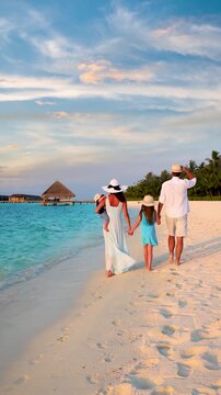 A elegant family on vacations walks down a tropical paradise beach in the Maldives islands during sunset time