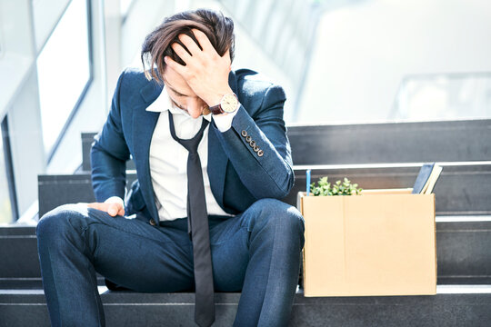 Depressed businessman sitting on stairs with belongings in cardboard box beside him