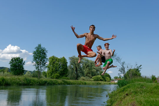 Germany, Bavaria, two teenage boys and man jumping into River Loisach