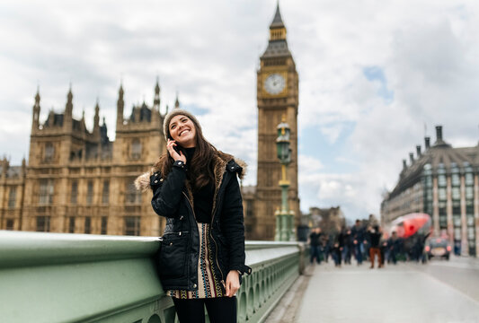 UK, London, happy young woman telephoning with smartphone in front of Palace of Westminster