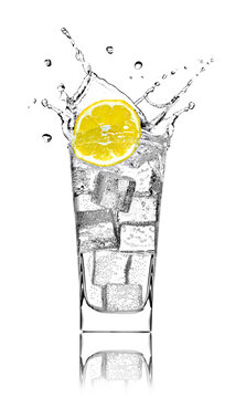 Glass with soda water, ice cubes and slice of lemon in front of white background