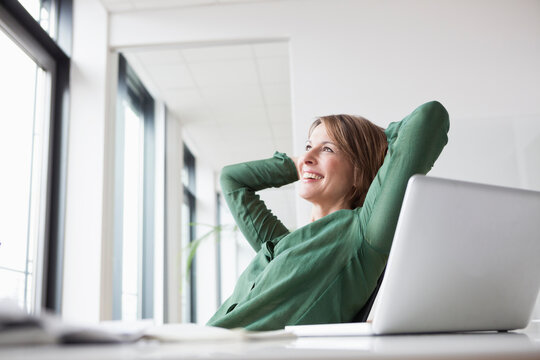 Smiling businesswoman at office desk leaning back