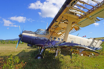 a crashed plane in the middle of a field. An abandoned biplane on the territory of the old airport. The plane with peeling paint is standing in tall grass, the upper wing is partially destroyed.  © nina blez