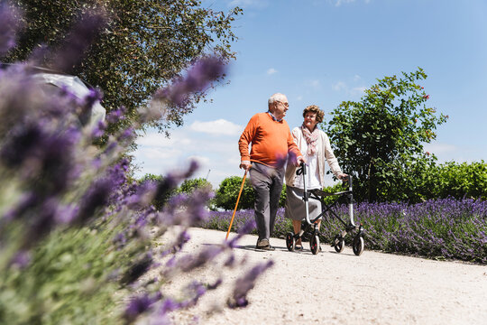 Senior couple walking in park, woman using wheeled walker