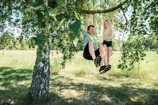 Father and daughter hanging on a branch of a birch tree