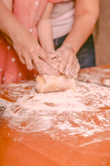 Fototapeta premium Hands of adult and child kneading dough on wooden kitchen table