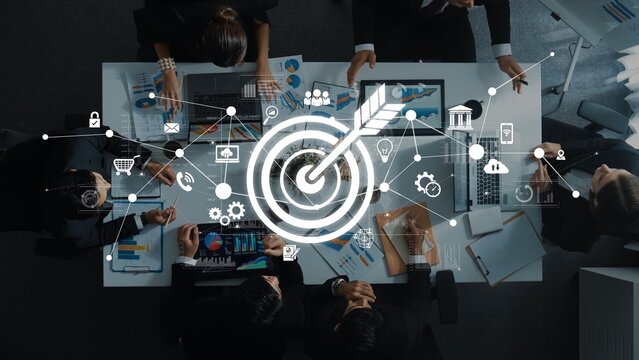 A top-down view of a business meeting where professionals collaborate on strategic goals, illustrated by digital icons representing innovation and marketing insights. Raster