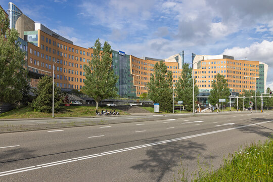 Amstelveen, Netherlands, 13 May 2026. Wide angle shot of the unique curved KPMG headquarters building facade framed by an asphalt road, green grass, and electric scooters.