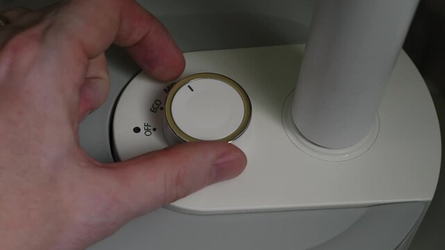 A man's hand turns a round knob on the control panel of a home appliance. Turning on the device and switching the mechanical dial to ECO and MID power modes