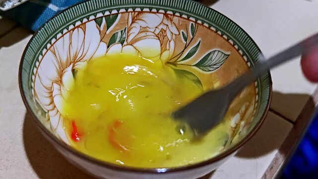Whisking Raw Eggs with Sliced Chili Peppers in a Ceramic Bowl