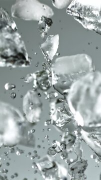 Pieces of ice with splashes of water soar up and fall. On a gray background. Filmed on a high-speed camera at 1000 fps.
