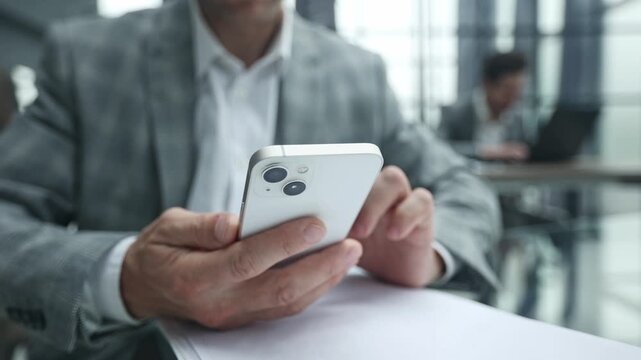 Man holds smartphone while seated at office table