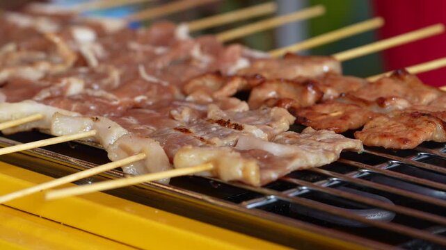 The shot of a cook grill Moo Ping or grilled pork skewers in Thai style on the yellow electric barbeque grill at the restaurant.