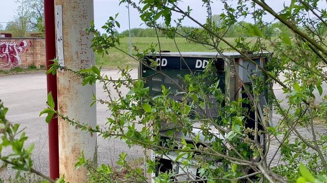 Old DD petrol dispenser overgrown with tree branches at abandoned filling station