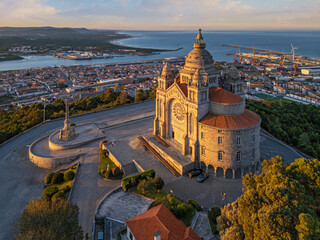 Wide drone view of Santa Luzia sanctuary at sunrise with Viana do Castelo, the Atlantic coast, port facilities, and a luminous hilltop forecourt. © Dmitry Rukhlenko