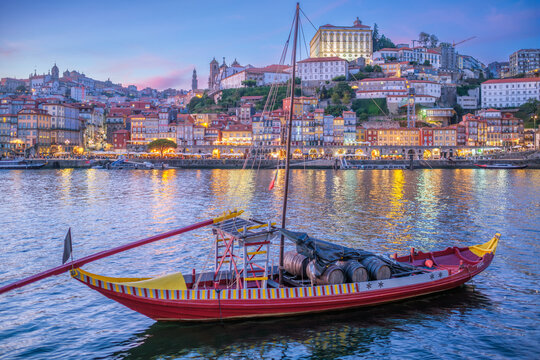 Evening rabelo boat on the Douro River near Porto Ribeira, Portugal, with sunset reflections and Vila Nova de Gaia riverfront architecture
