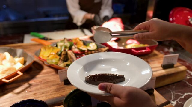 Person Serving Grilled Vegetables and Roast Ham at a Buffet