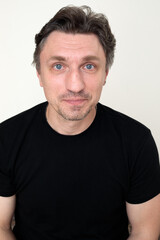 Obraz premium close up portrait of middle aged man with raised eyebrows and surprised expression in black t-shirt looking at camera, white background headshot