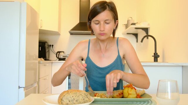 Woman sits at kitchen table eating stuffed paprika, enjoying homemade Balkan cuisine, turning meal into cultural moment shared in quiet domestic space.