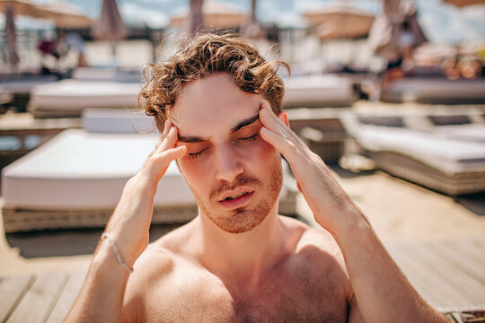 Young hot man resting alone. Sick ill guy had headache or pain. Covid-19 coronavirus symptoms. Sit alone and suffer outside under sun. Sickness.