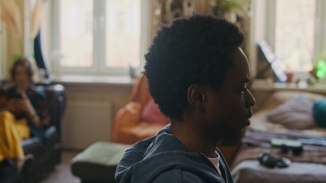 Pan shot of two diverse roommates living together, gen Z Caucasian woman resting on couch with smartphone, African American freelancer coding on computer